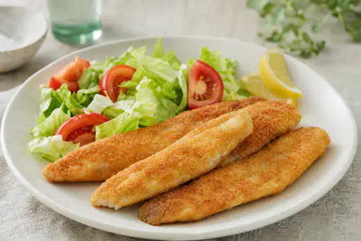 Filetes de bacaladilla rebozados y dorados sobre un plato con ensalada de lechuga y una cuña de limón