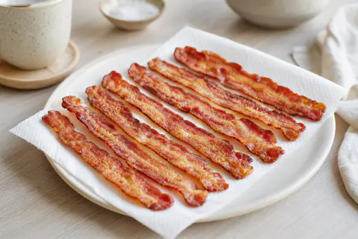 Lonchas de bacon crujiente y doradas colocadas sobre papel de cocina en un plato