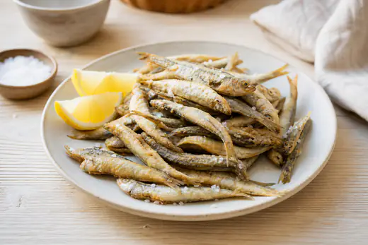 Plato de boquerones fritos enharinados, dorados y crujientes, con cuñas de limón y un poco de sal