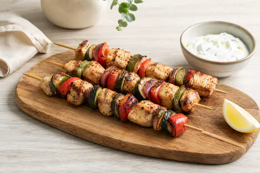 Brochetas de pollo con pimiento rojo y verde, cebolla y calabacín, doradas, sobre una tabla con limón