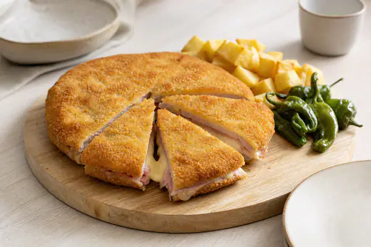 Cachopo individual redondo, dorado y empanado, cortado en cuñas con queso fundido y jamón, con patatas fritas