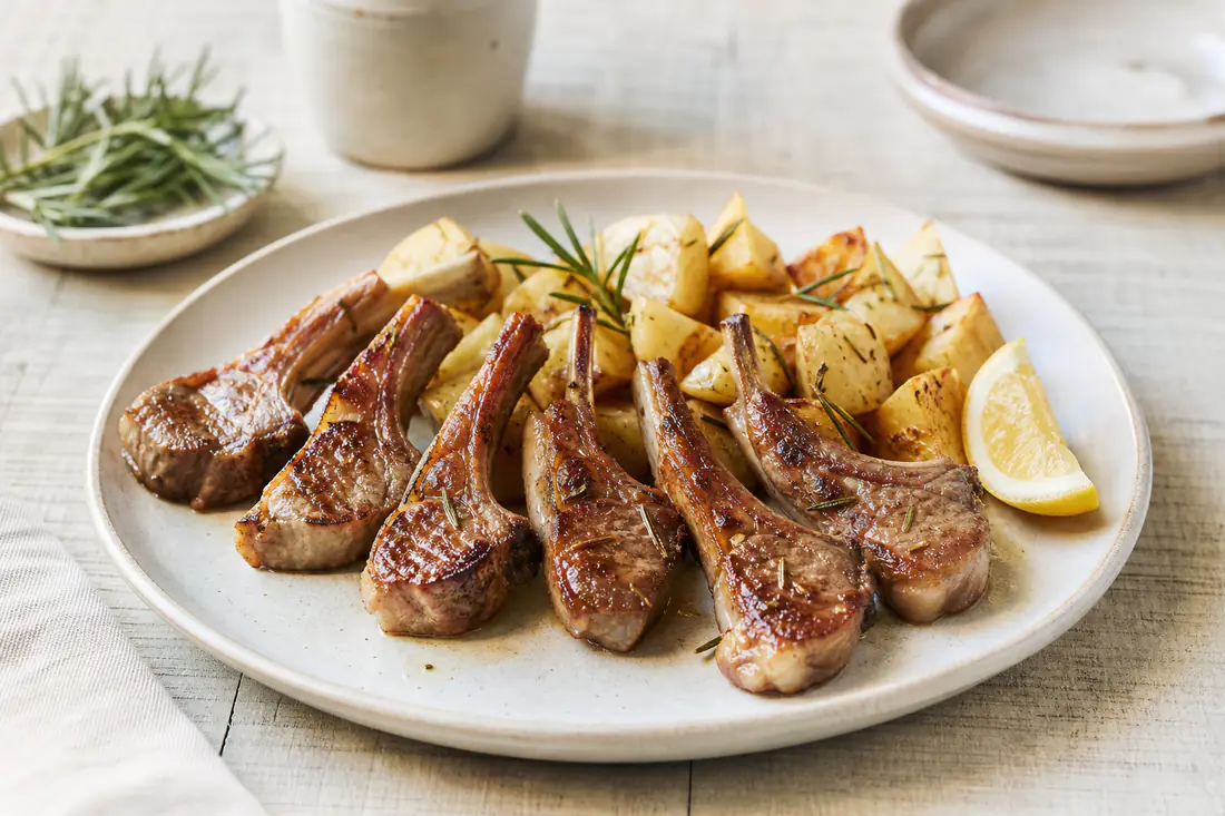 Chuletillas de cordero lechal doradas con hueso, servidas con patatas panadera y ramitas de romero