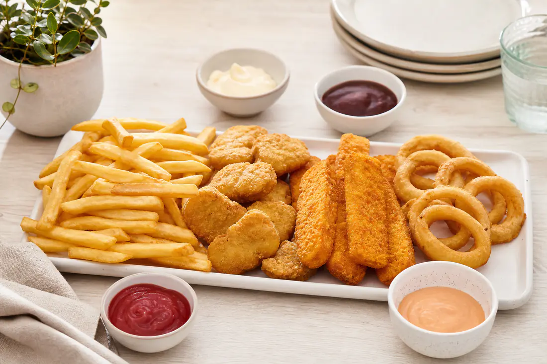 Patatas fritas, nuggets y palitos de pescado dorados recién salidos de la cesta de una freidora de aire