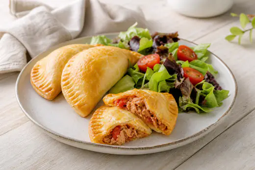 Empanadillas de atún doradas con el borde sellado con tenedor, una abierta mostrando el relleno de atún y tomate