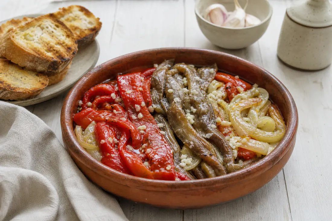 Escalivada con tiras de berenjena, pimiento rojo y cebolla asados, aliñados con aceite de oliva y ajo, en una fuente de barro