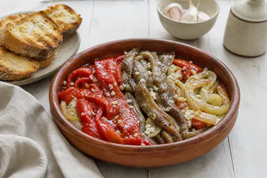 Escalivada con tiras de berenjena, pimiento rojo y cebolla asados, aliñados con aceite de oliva y ajo, en una fuente de barro