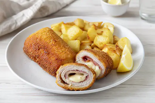 Flamenquines cordobeses dorados y crujientes, uno cortado para mostrar el jamón y el queso, con patatas y limón