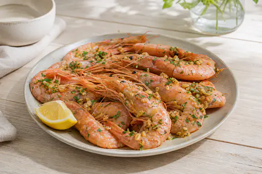 Plato de gambas rosadas con cáscara, ajo dorado y perejil, acompañado de una cuña de limón