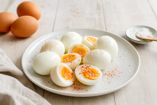 Huevos cocidos pelados y partidos por la mitad con la yema cremosa, sobre un plato blanco con sal y pimentón