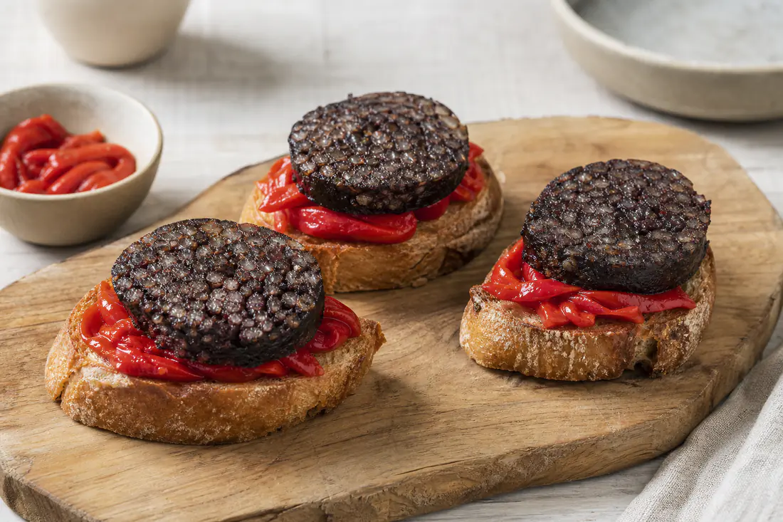 Rodajas de morcilla de Burgos con arroz, doradas y crujientes, sobre rebanadas de pan tostado con pimientos del piquillo