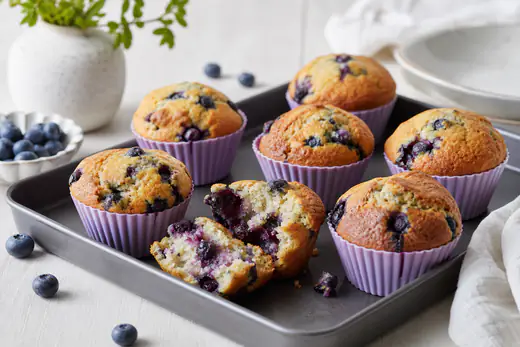 Muffins de arándanos con la parte superior dorada y arándanos visibles, en cápsulas de silicona sobre una bandeja