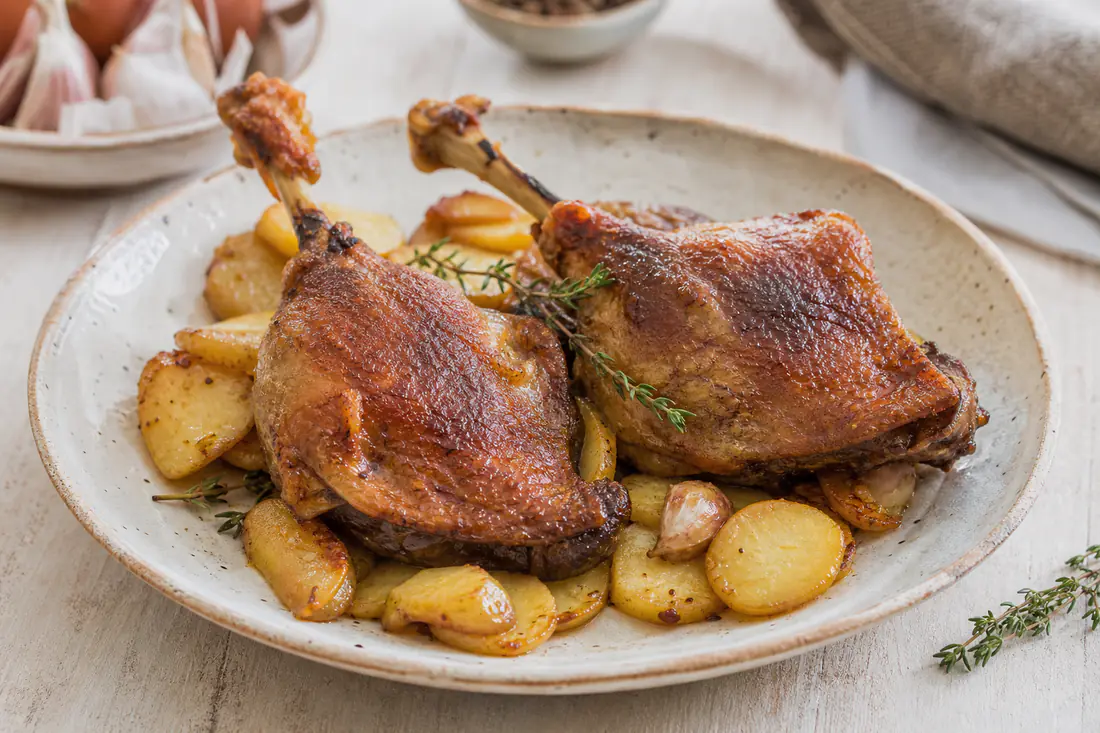 Muslo de pato con la piel dorada y crujiente servido sobre patatas salteadas con una ramita de tomillo