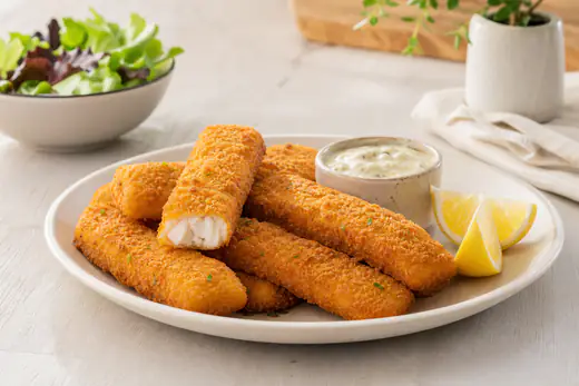 Plato de palitos de pescado empanados, dorados y crujientes, con un cuenco de salsa tártara y cuñas de limón