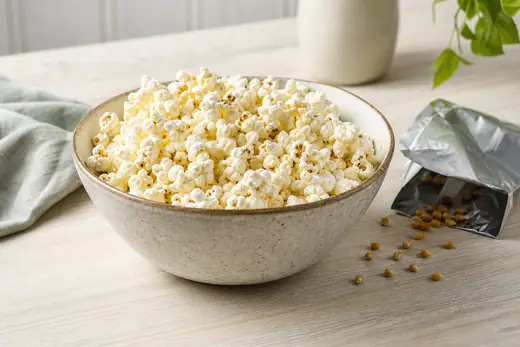 Un bol grande de palomitas recién hechas, algunas con granos sin abrir en el fondo, junto a un paquete de papel de aluminio abierto