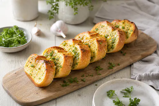 Baguette de pan de ajo dorada y cortada en rebanadas, con mantequilla y perejil picado, sobre una tabla de madera