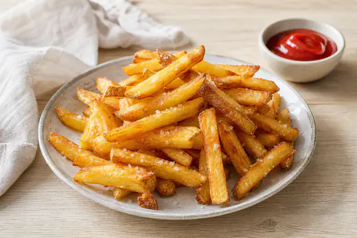 Plato de patatas fritas caseras en bastones, doradas y crujientes, con sal gruesa y un cuenco de kétchup al lado