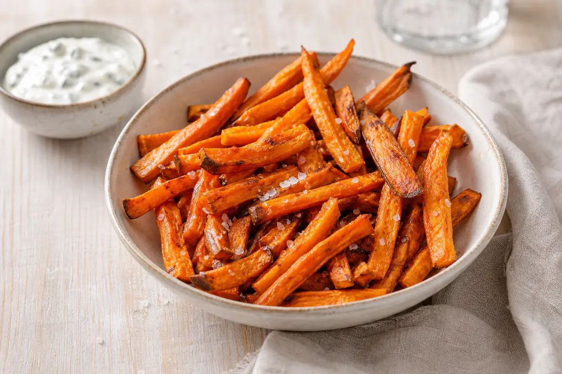 Bastones de boniato naranja, dorados y crujientes, servidos en un cuenco con sal en escamas y una salsa de yogur