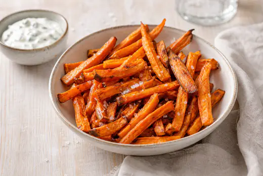 Bastones de boniato naranja, dorados y crujientes, servidos en un cuenco con sal en escamas y una salsa de yogur