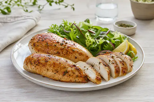 Dos pechugas de pollo enteras doradas, una de ellas cortada en lonchas para mostrar el interior jugoso, con ensalada