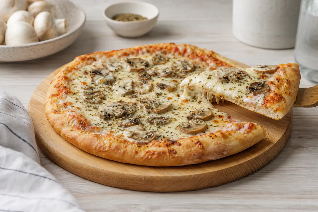 Pizza casera pequeña y redonda con mozzarella fundida, champiñones laminados y orégano, sobre una tabla de madera