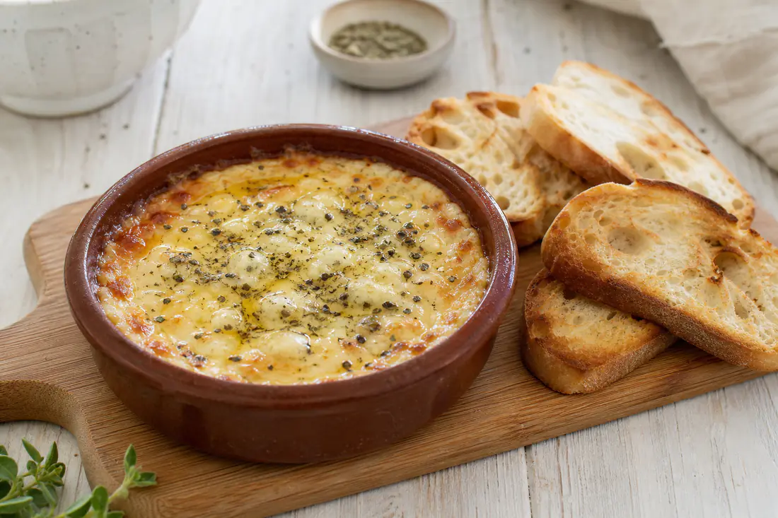 Provoleta fundida y dorada en una cazuelita de barro, con orégano y pimienta, junto a rebanadas de pan tostado