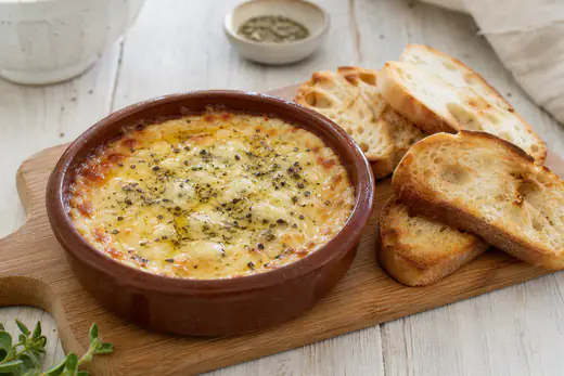 Provoleta fundida y dorada en una cazuelita de barro, con orégano y pimienta, junto a rebanadas de pan tostado