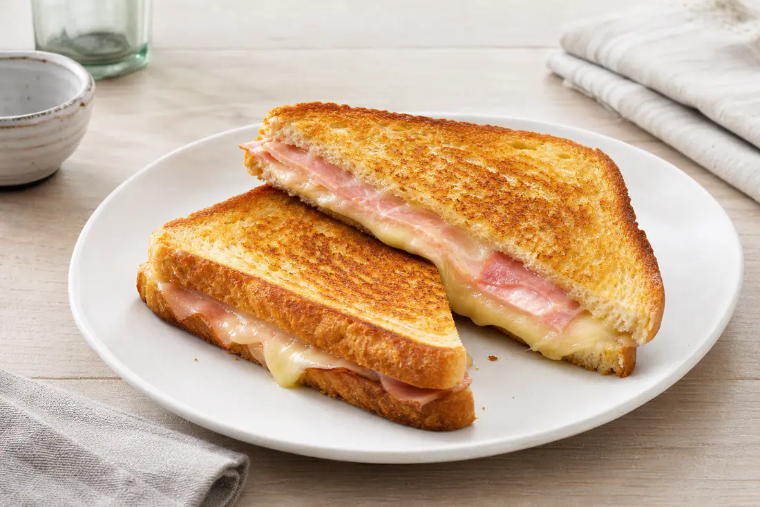 Dos sándwiches mixtos dorados cortados en diagonal, con jamón york y queso fundido, en un plato blanco