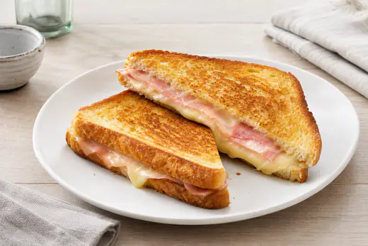 Dos sándwiches mixtos dorados cortados en diagonal, con jamón york y queso fundido, en un plato blanco