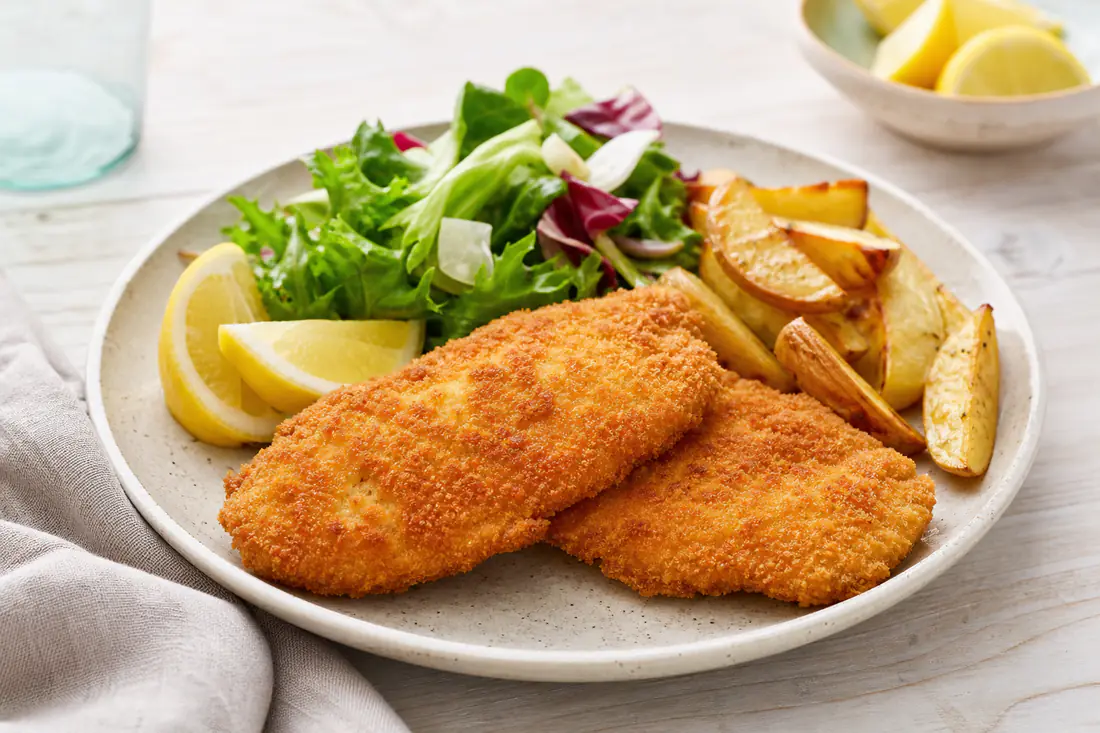 Filetes de pollo empanados, dorados y crujientes, servidos con rodajas de limón, ensalada y patatas