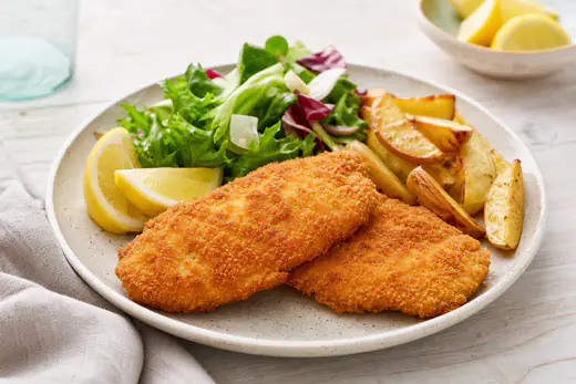 Filetes de pollo empanados, dorados y crujientes, servidos con rodajas de limón, ensalada y patatas