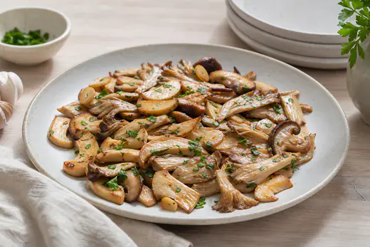 Mezcla de setas de cardo en láminas, setas de ostra y shiitake doradas, con ajo laminado y perejil picado en un plato de cerámica