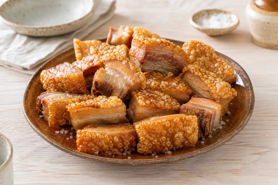 Torreznos de Soria dorados con la corteza ampollada y crujiente, servidos en un plato de barro con sal en escamas