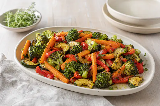 Fuente de verduras asadas con zanahoria, calabacín, pimiento rojo y brócoli doradas, con hierbas y aceite de oliva