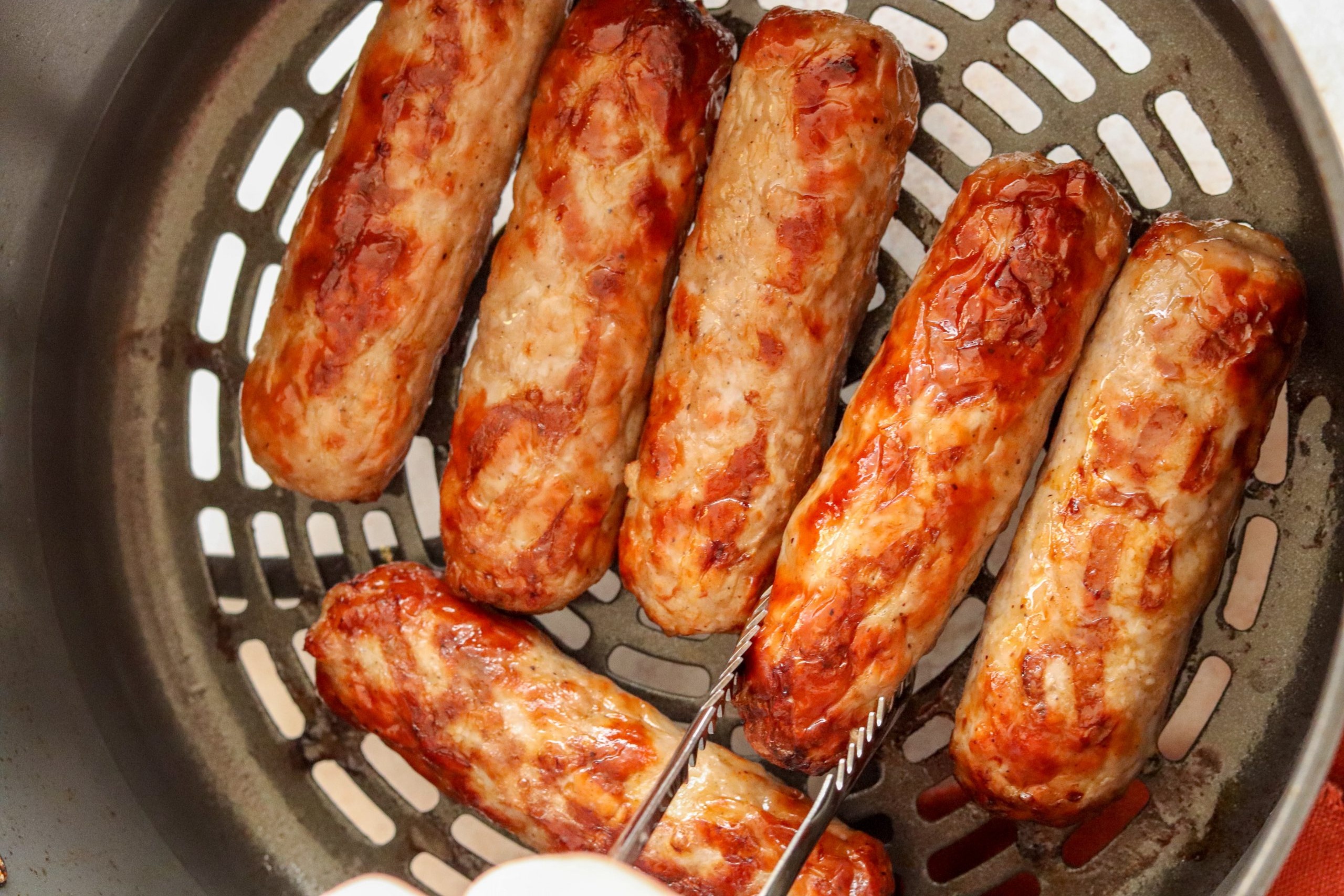 Salchichas doradas cocinadas en freidora de aire servidas en un plato blanco.